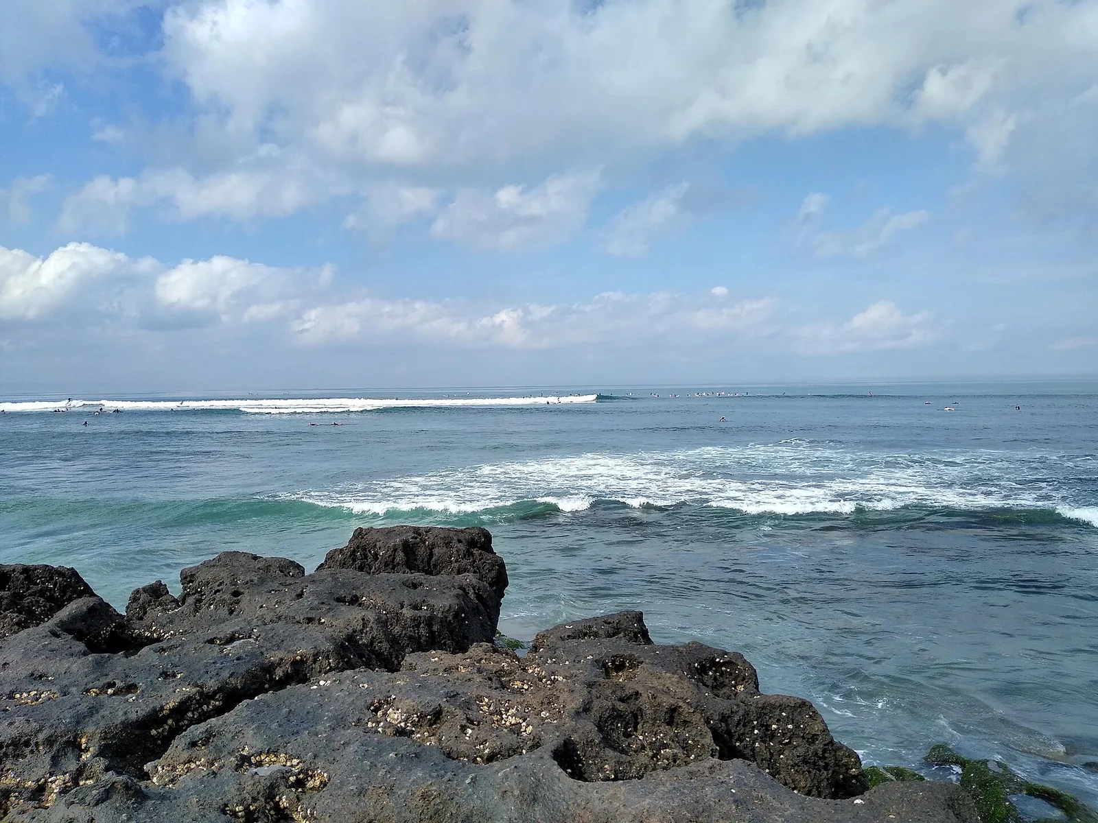 Wellen des Indischen Ozeans auf dem vulkanischen Gestein am Strand von Canggu, unter blauem Himmel