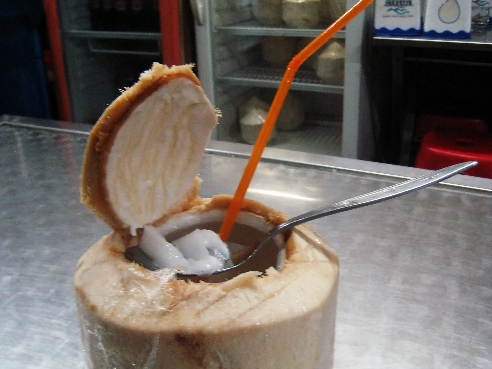 Noix de coco ouverte servie avec une paille, l’eau et la chair à l’intérieur