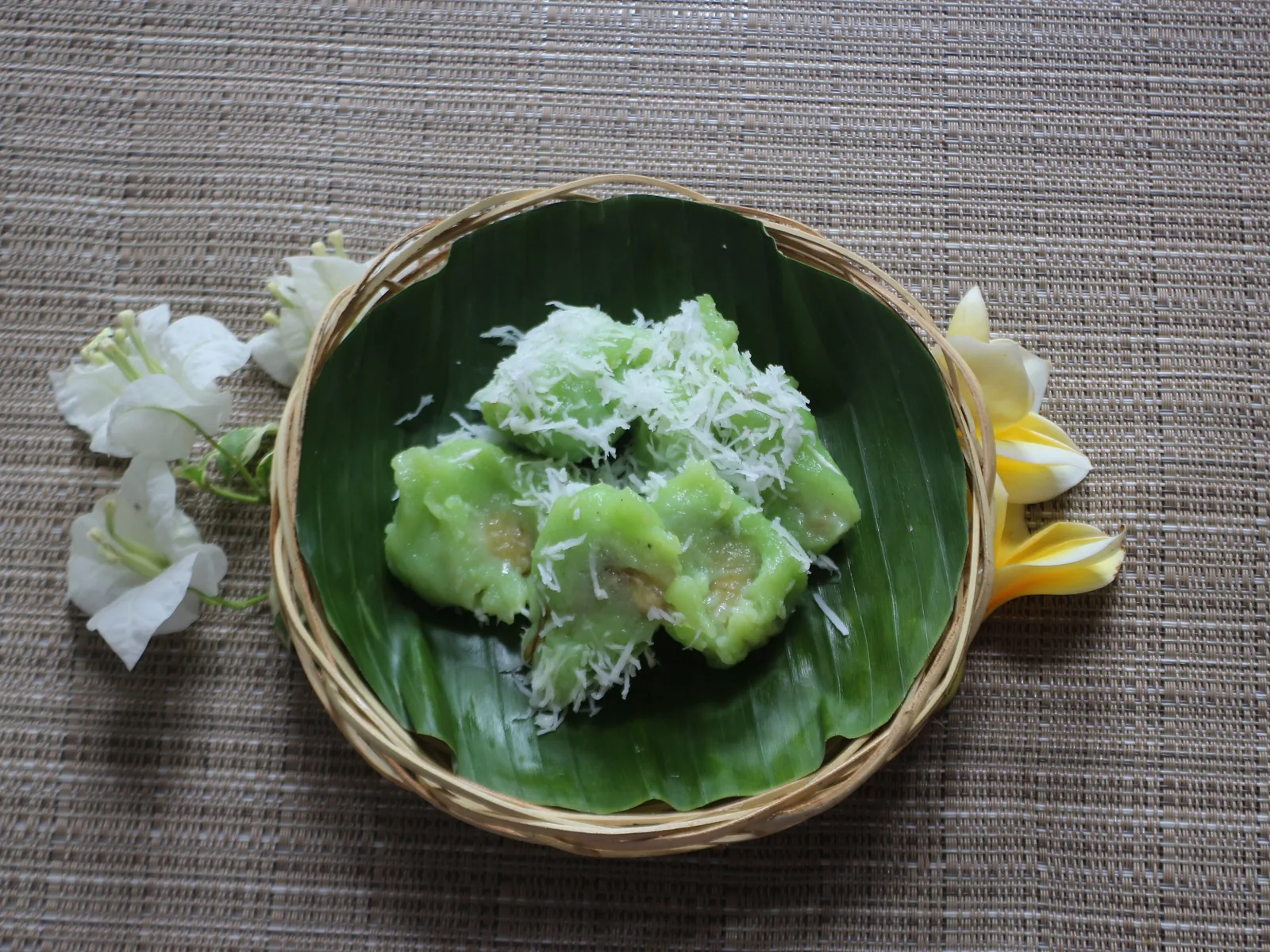Pisang rai verts roulés dans la noix de coco râpée, présentés dans une corbeille sur une feuille de bananier