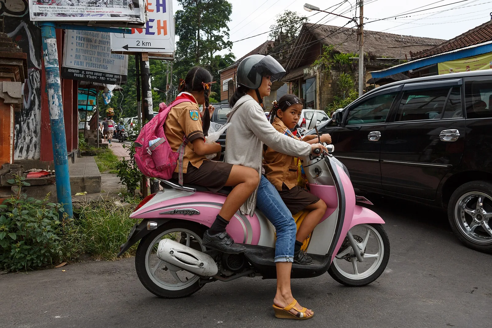 Drei Mitfahrende auf einem rosa Roller auf der Hauptstraße von Ubud